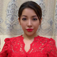 Burmese model Nang Mwe San in a red dress stands in front of a curtain holding up three fingers and touching thumb to pinky finger.